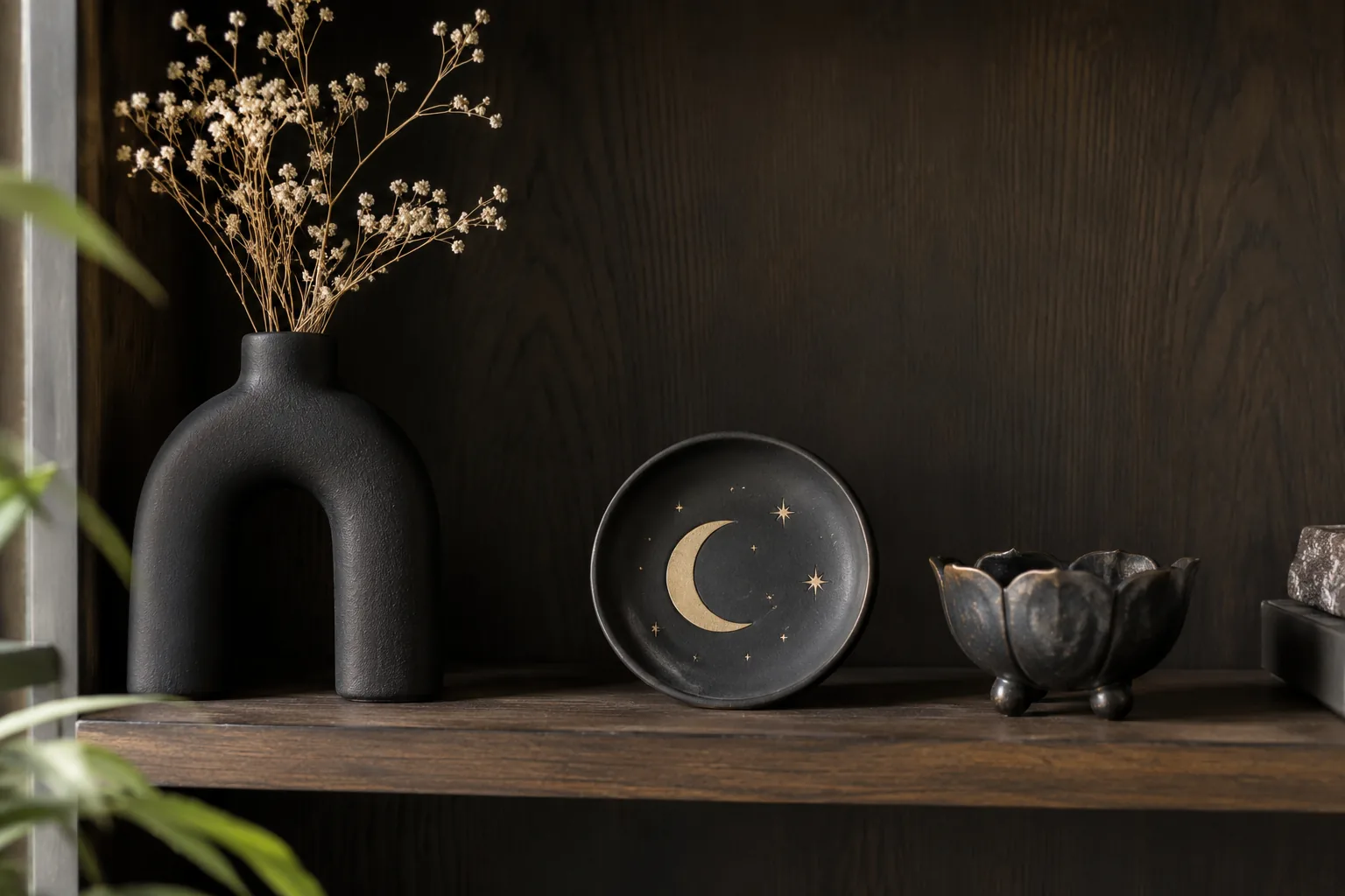 Quiet dark wood shelf displaying three unique gothic-inspired matte ceramic objects with generous open space, black arch vase, moon dish and small sculptural bowl